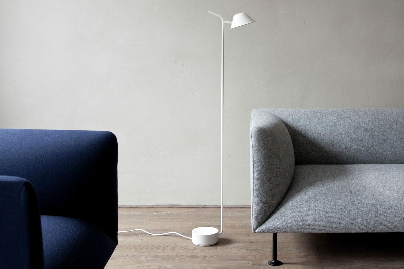 Minimal floor lamp positioned beside a contemporary sofa in a luxury residential living room, creating warm ambient illumination.