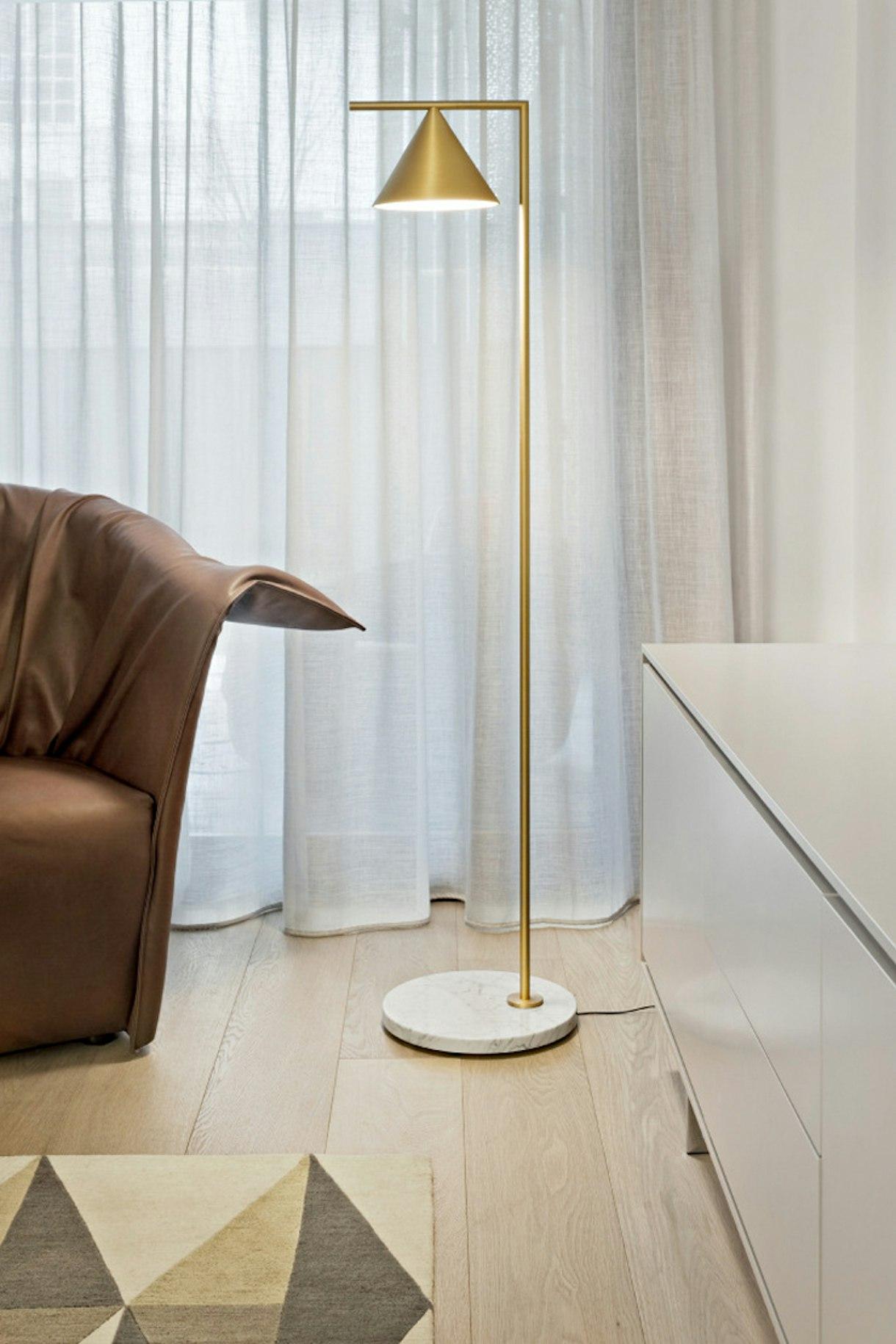 Minimal floor lamp positioned beside a contemporary sofa in a luxury residential living room, creating warm ambient illumination.