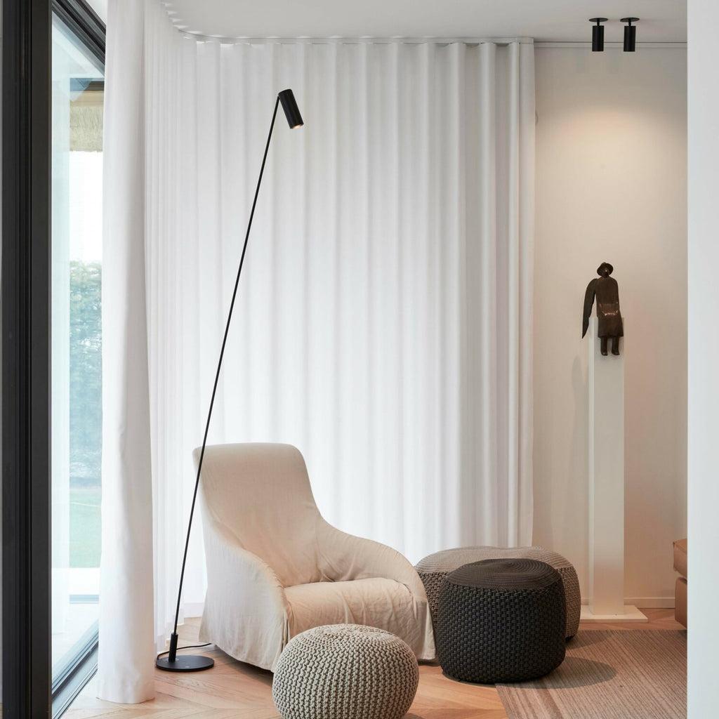 Minimal floor lamp positioned beside a contemporary sofa in a luxury residential living room, creating warm ambient illumination.
