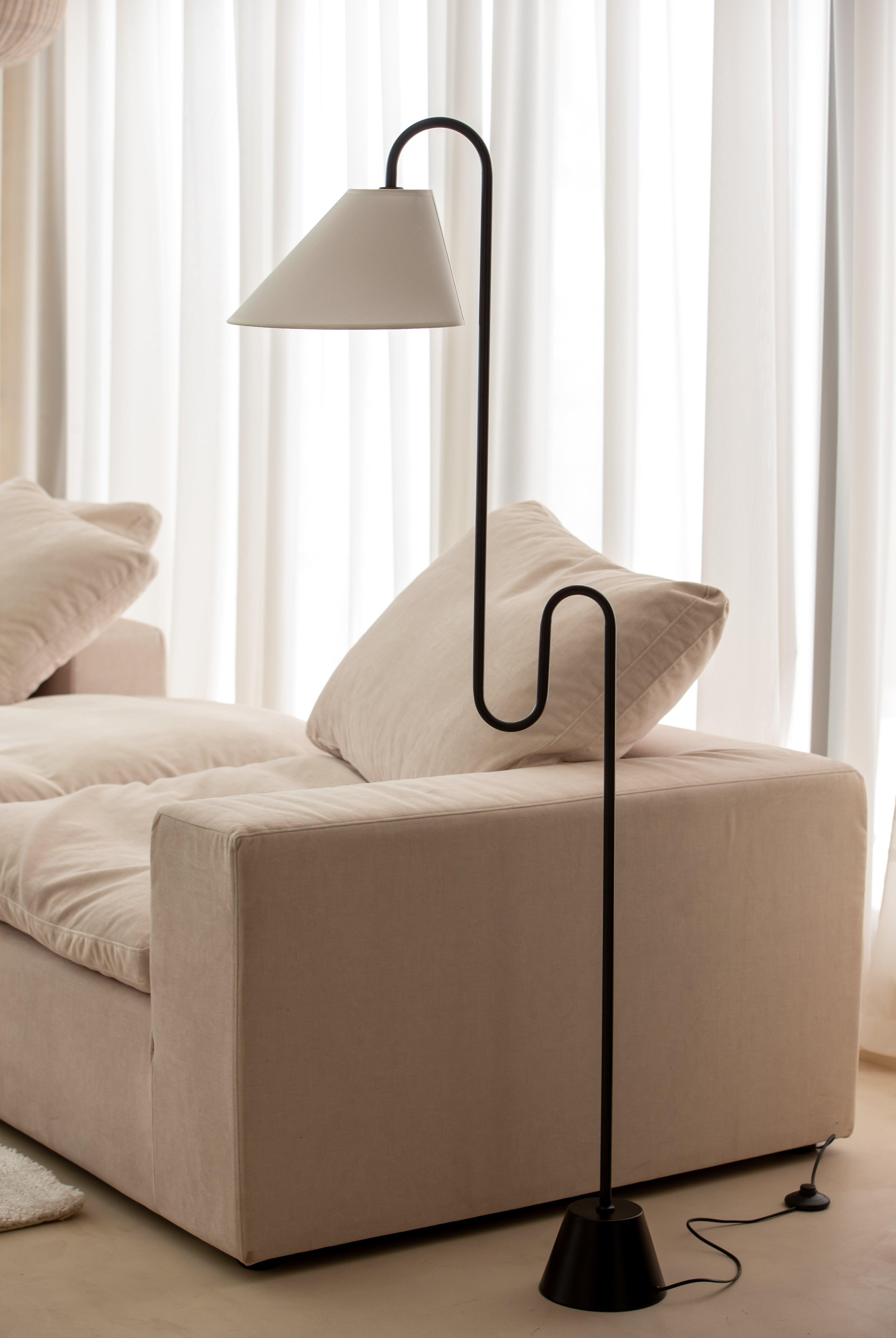 Minimal floor lamp positioned beside a contemporary sofa in a luxury residential living room, creating warm ambient illumination.