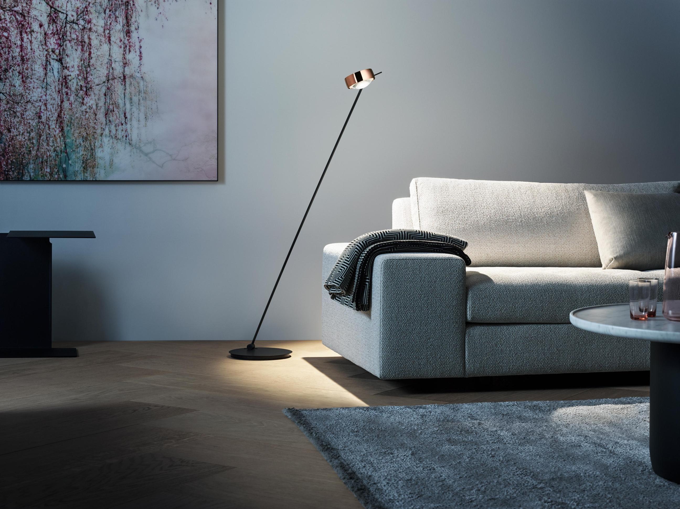 Minimal floor lamp positioned beside a contemporary sofa in a luxury residential living room, creating warm ambient illumination.