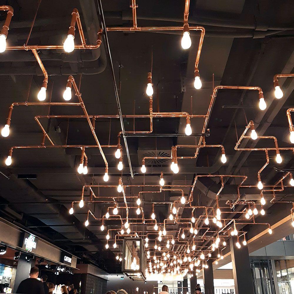 A pipe-based decorative ceiling light combining exposed metal fittings with warm filament bulbs.