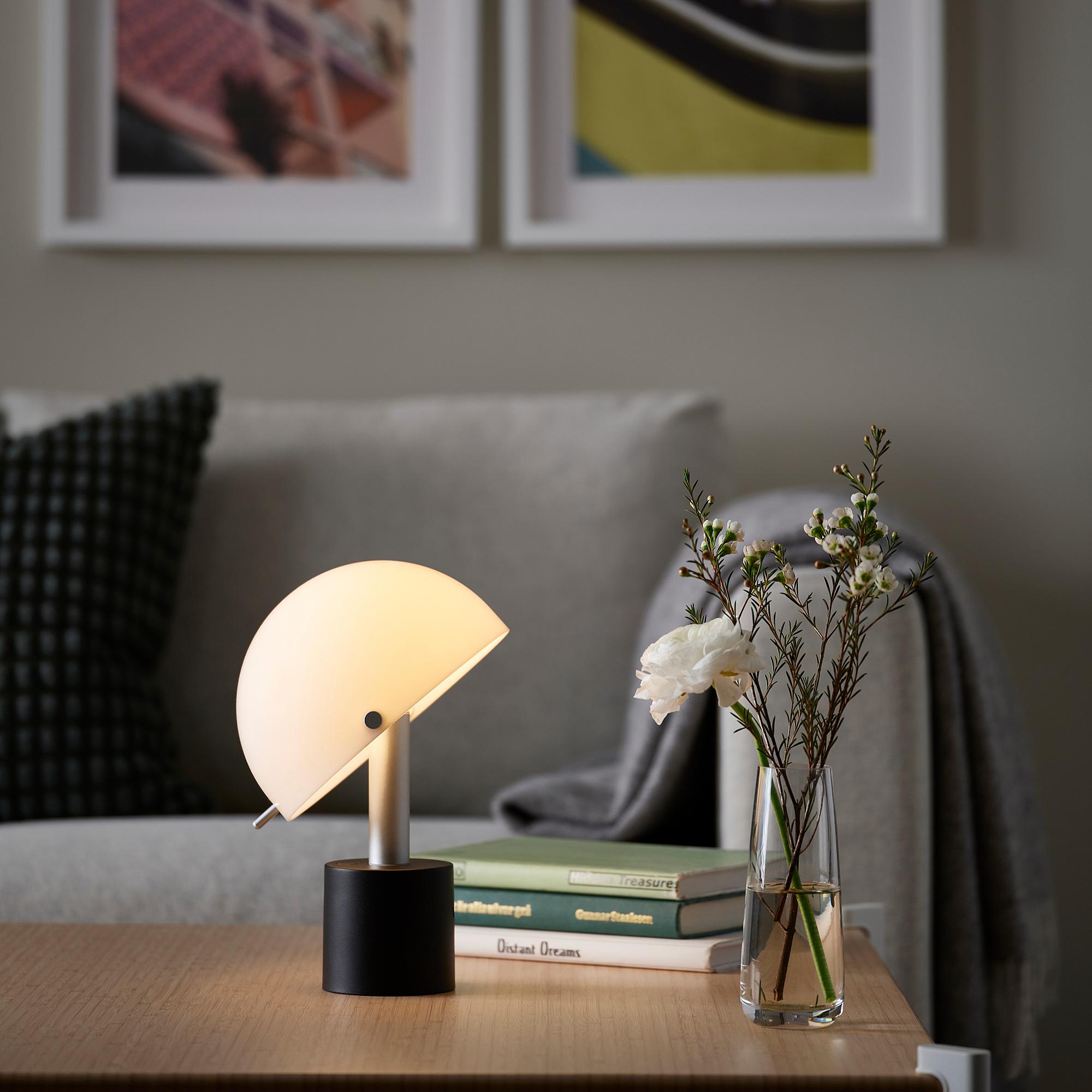 Scandinavian table lamp placed on a wooden side table in a bright contemporary living room, creating warm and comfortable ambient lighting.