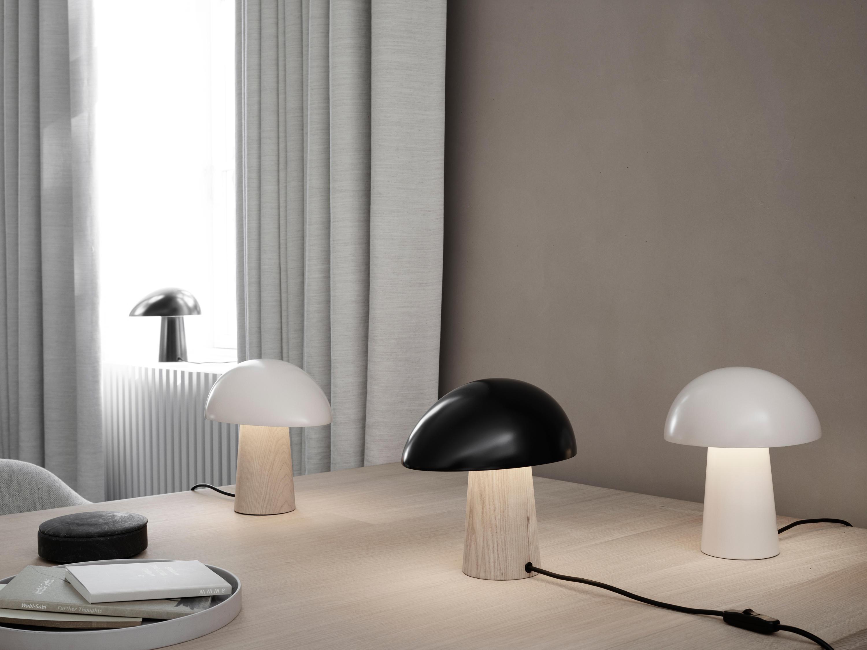 Scandinavian table lamp placed on a wooden side table in a bright contemporary living room, creating warm and comfortable ambient lighting.