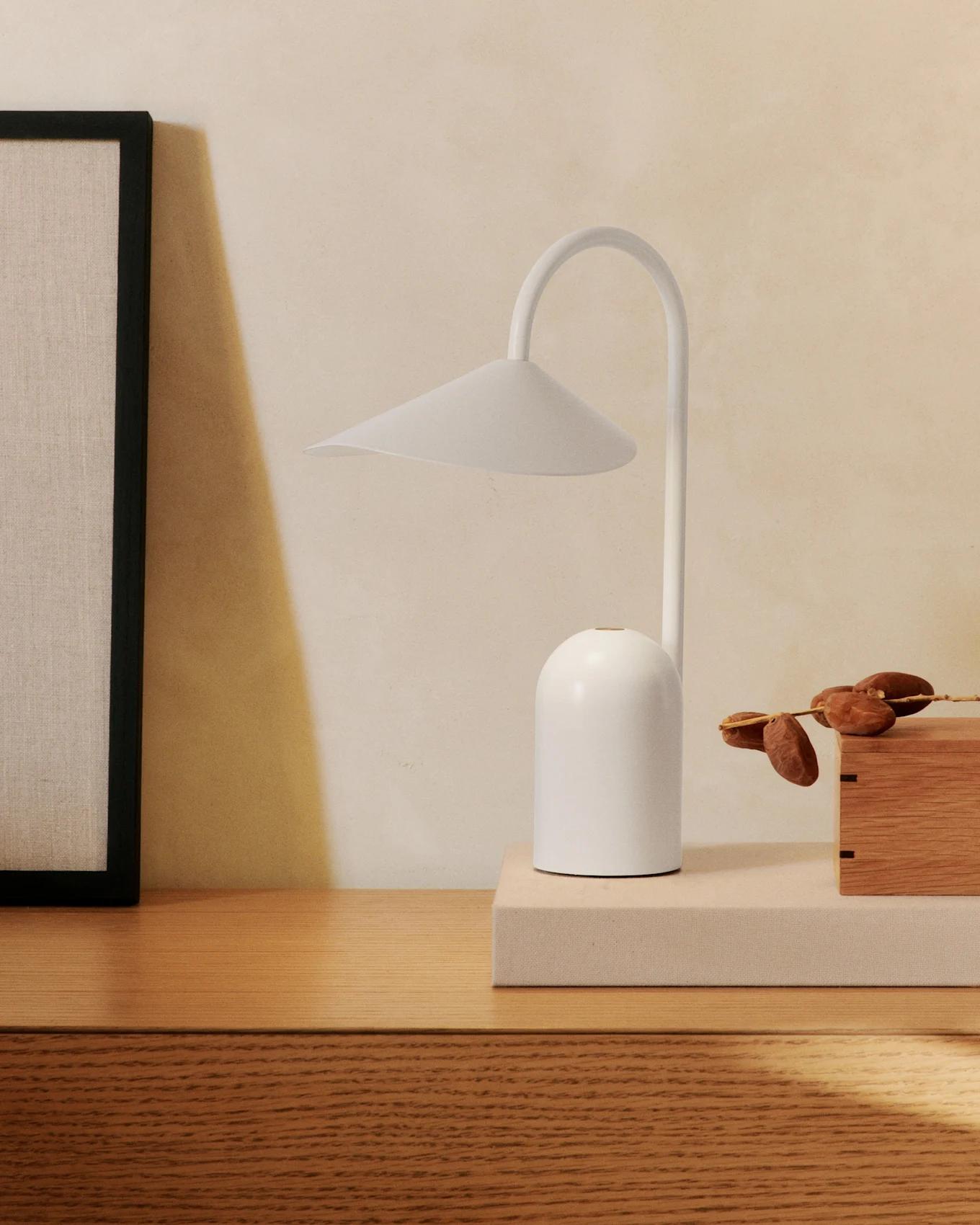 Scandinavian table lamp placed on a wooden side table in a bright contemporary living room, creating warm and comfortable ambient lighting.