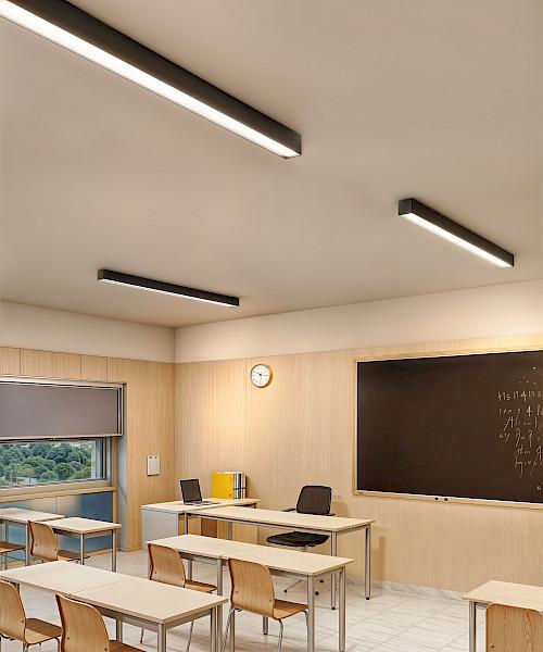 Surface-mounted linear lights providing uniform illumination across a classroom blackboard.