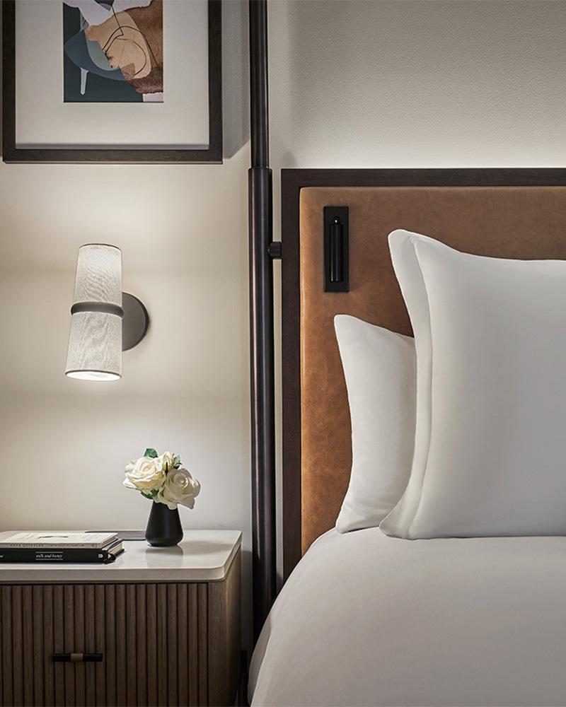 Bedside wall lamp installed beside a luxury hotel bed providing warm ambient illumination.