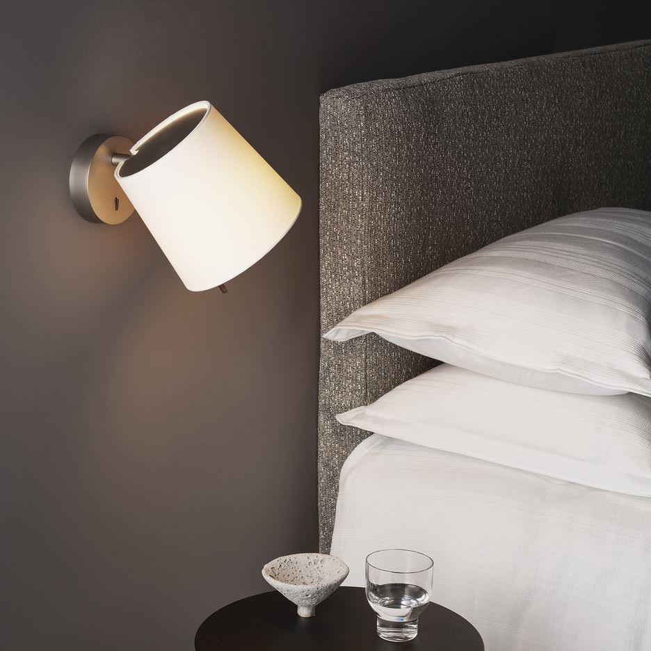 Bedside wall lamp installed beside a luxury hotel bed providing warm ambient illumination.