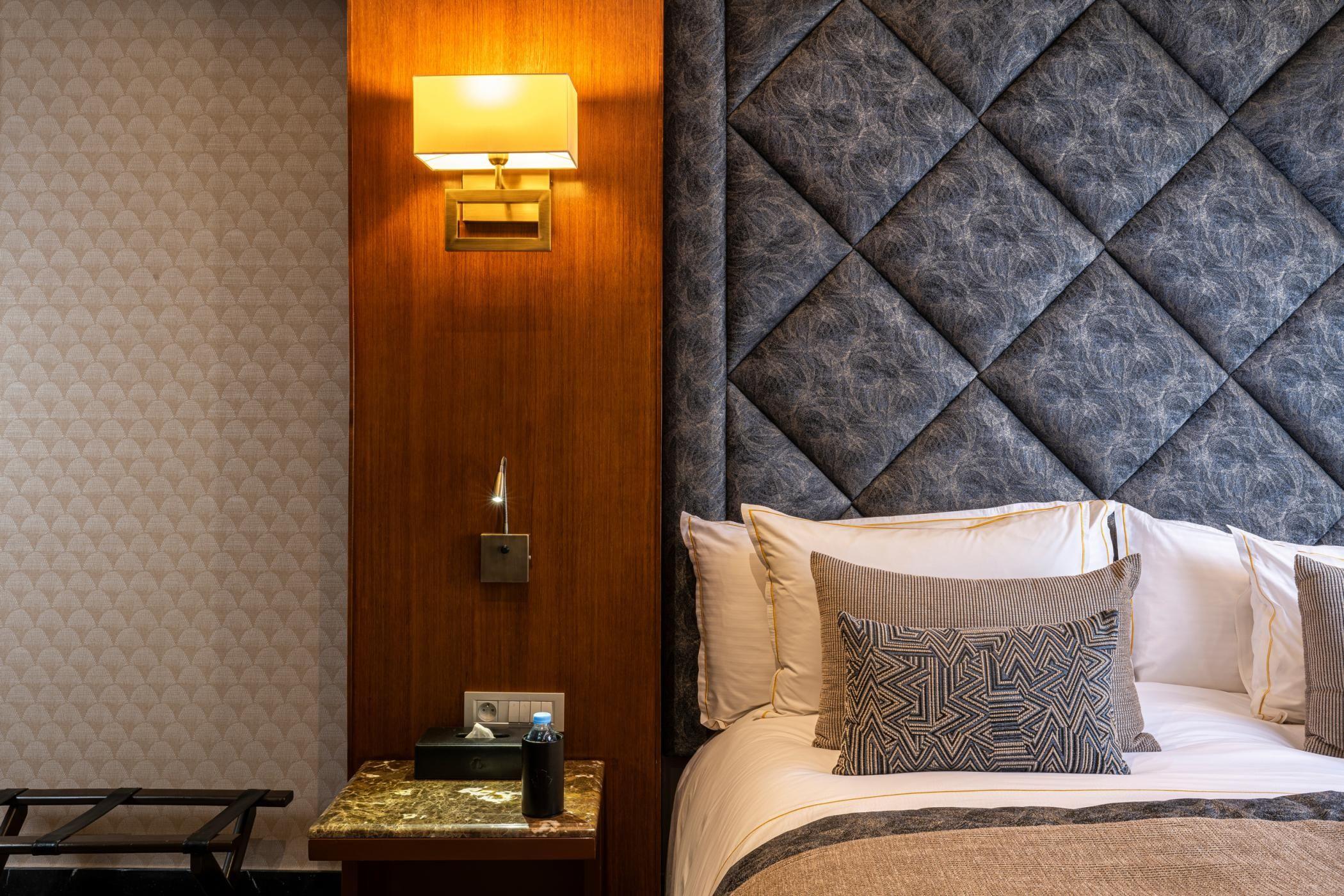 Bedside wall lamp installed beside a luxury hotel bed providing warm ambient illumination.