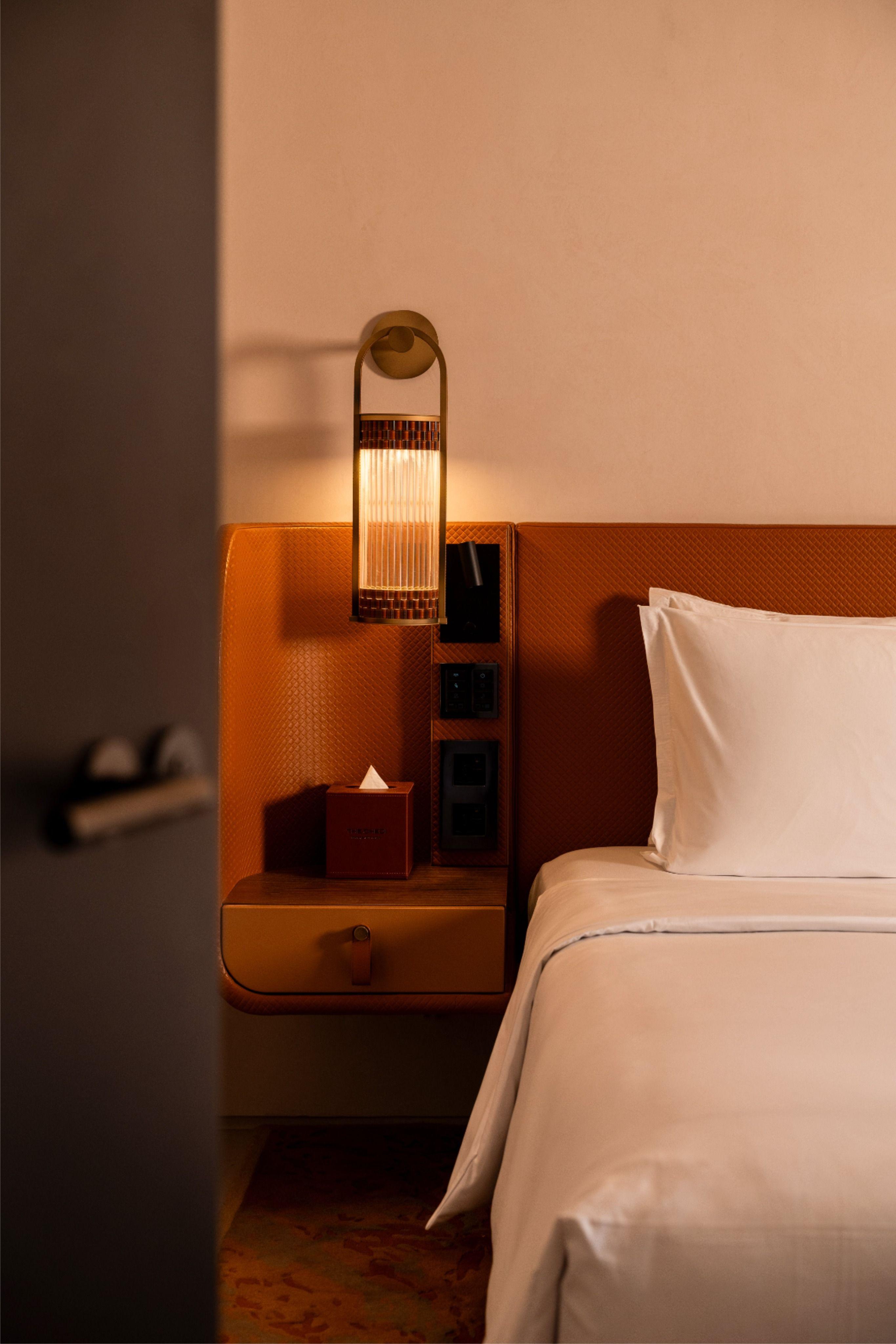 Bedside wall lamp installed beside a luxury hotel bed providing warm ambient illumination.