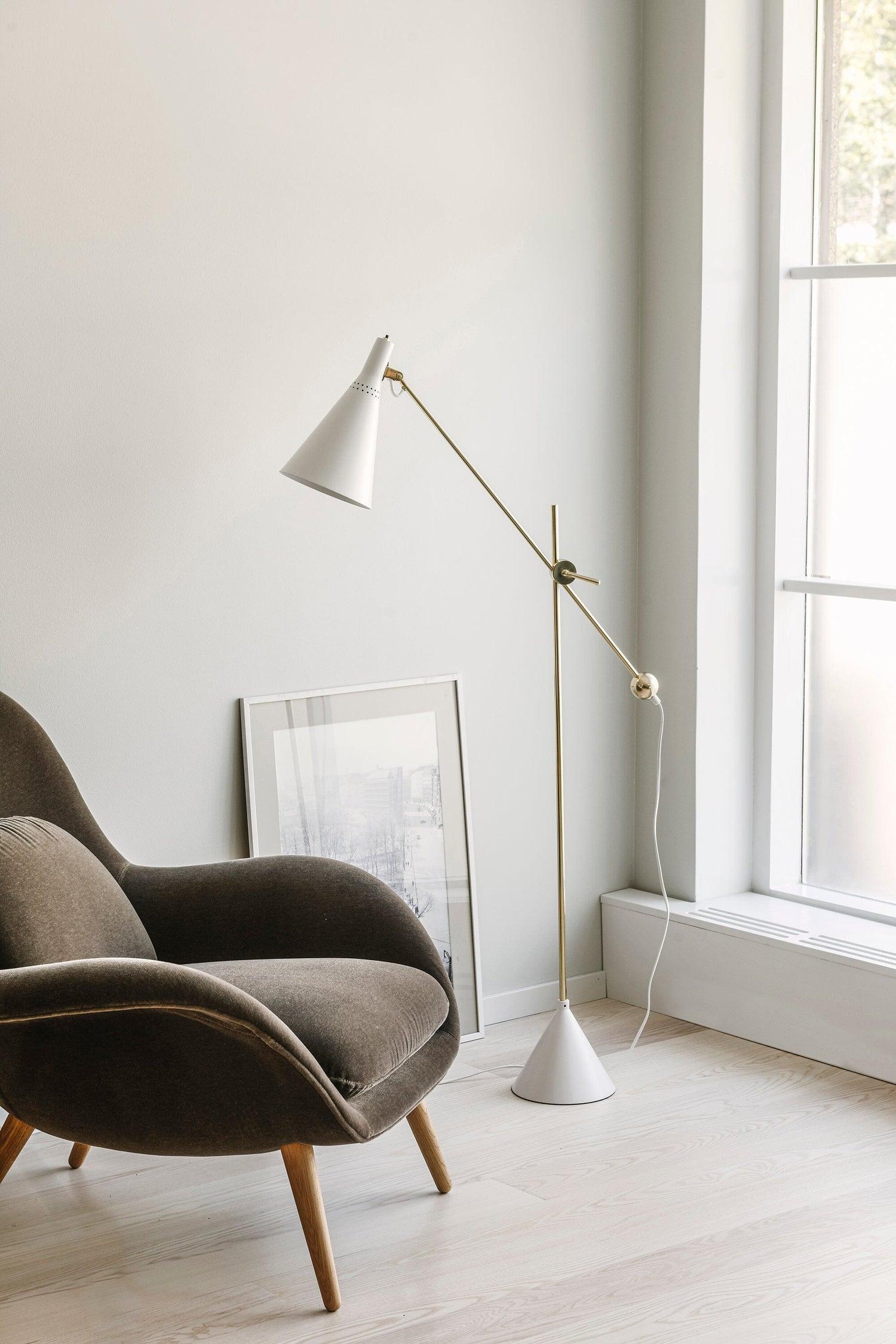 Scandinavian floor lamp positioned beside a lounge chair in a bright contemporary living room, creating warm and comfortable ambient lighting.