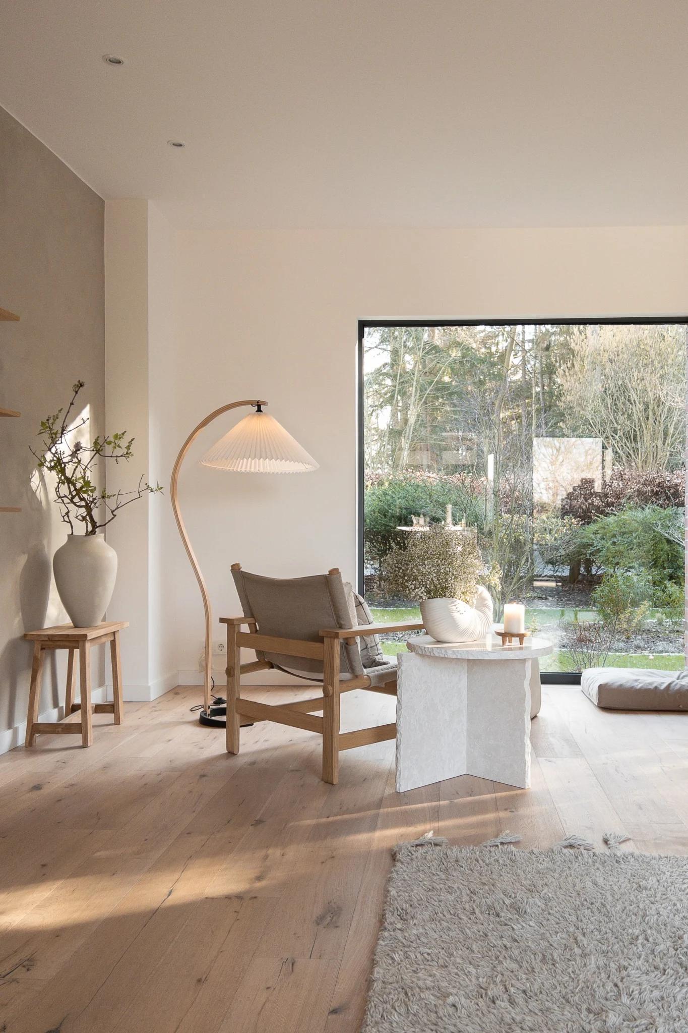 Scandinavian floor lamp positioned beside a lounge chair in a bright contemporary living room, creating warm and comfortable ambient lighting.