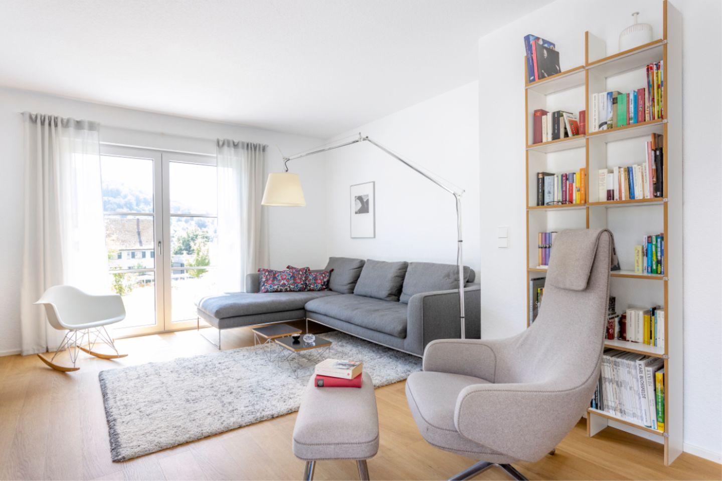 Scandinavian floor lamp positioned beside a lounge chair in a bright contemporary living room, creating warm and comfortable ambient lighting.