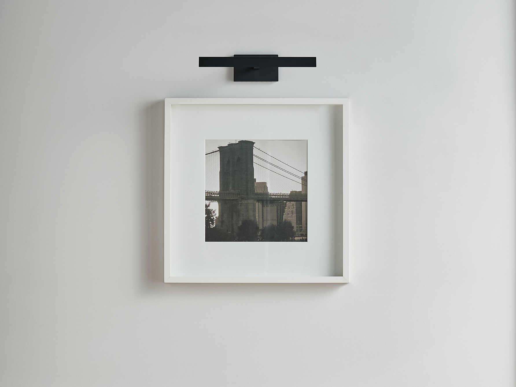 Picture wall lamp illuminating artwork inside a luxury gallery and hospitality interior.