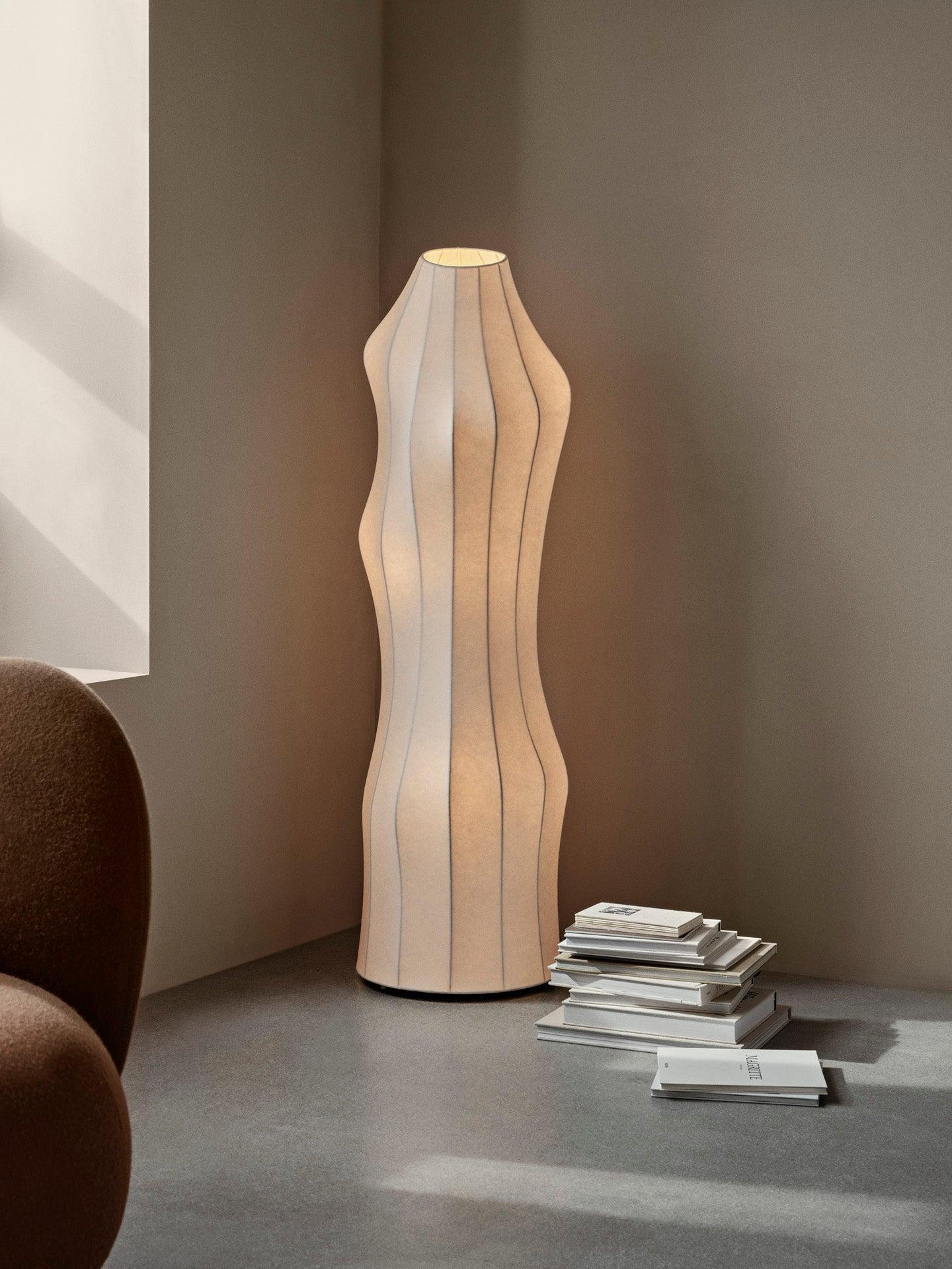 Organic floor lamp positioned beside a lounge chair in a contemporary residential living room creating warm ambient lighting and a calm natural atmosphere.