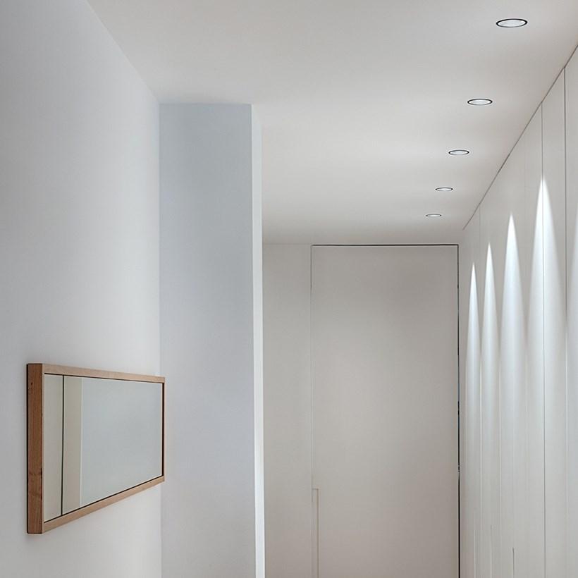 Asymmetric recessed downlights providing directional illumination along a wall in a contemporary interior.