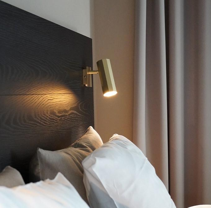 Reading wall lamp installed beside a luxury hotel bed providing comfortable task illumination.